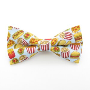 May include: A blue bow tie featuring a pattern of various fast food items, including hot dogs, hamburgers, chips, pizza, and popcorn.