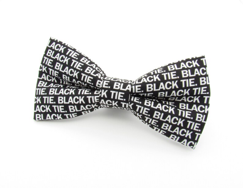 May include: A black bow tie featuring a repeating white text pattern that reads BLACK TIE. The bow tie has a classic shape with a central knot and two symmetrical wings, displaying the white sans-serif lettering clearly against the dark fabric.