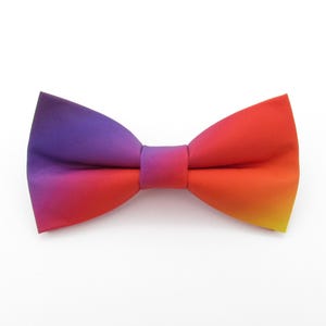 May include: A colorful ombre bow tie with a gradient of purple, pink, orange, and yellow.
