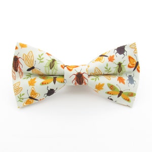 May include: A white bow tie featuring a pattern of butterflies and insects in shades of orange, brown, and green.