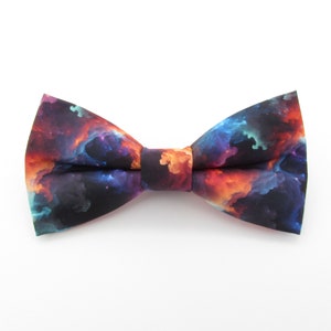 Puede incluir: Una pajarita negra con estampado de galaxia de colores. El estampado presenta tonos de naranja, rojo, azul y morado.