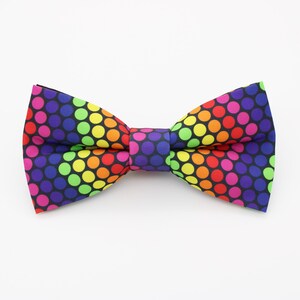 May include: A rainbow polka dot bow tie with a black background. The bow tie is made of fabric and has a classic bow tie shape.