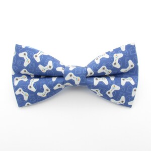 May include: A blue bow tie with a white pattern of video game controllers.