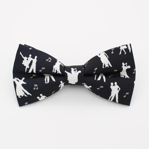 May include: A black bow tie featuring a white pattern of dancing figures and musical notes. This formal accessory is ideal for special occasions. The bow tie is a classic design.
