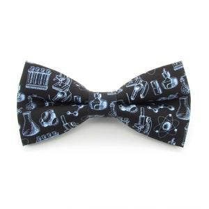 May include: A black bow tie with a repeating pattern of light blue science-themed illustrations, including beakers, microscopes, and atoms. The bow tie is a classic shape, suitable for formal or themed events.