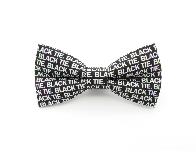 May include: A black bow tie featuring a repeating white text pattern that reads BLACK TIE. The bow tie has a classic pre-tied shape with a central knot and two symmetrical wings, constructed from a fabric with a crisp, high-contrast graphic design.