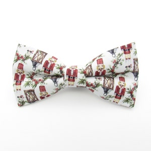 May include: A white bow tie with a festive Christmas pattern featuring nutcracker soldiers and lanterns.