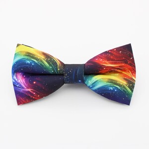 May include: A rainbow galaxy print bow tie with a black background. The bow tie is made of a soft, comfortable fabric and has a classic bow tie shape.