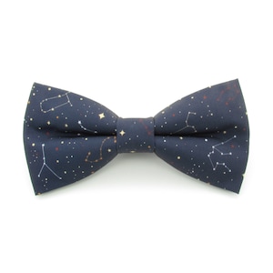Può includere: Un papillon blu navy con un motivo di costellazioni con stelle bianche, dorate e rosse. Questo accessorio classico è perfetto per aggiungere un tocco di stile a qualsiasi outfit. Il tessuto ha una leggera lucentezza.