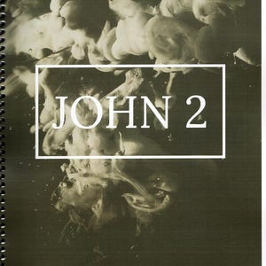 May include: A spiral-bound notebook with a dark, abstract design. The cover features a white rectangular frame with the text "JOHN 2" in bold, white letters. The background is a blend of dark and light tones, creating a smoky effect.