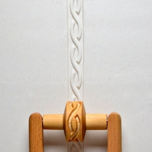 May include: A wooden rolling pin with a carved design. The rolling pin has handles on either side and a decorative pattern on the rolling surface.