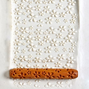 May include: A wooden rolling pin with a floral design. The rolling pin is used to create patterns in clay or dough.
