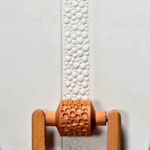 May include: A wooden rolling pin with a textured surface of small circles. The rolling pin has two wooden handles.