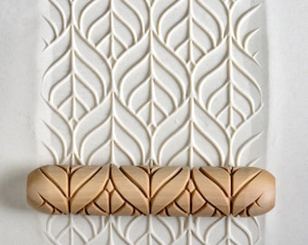 Op de afbeelding: Een houten deegroller met een herhalend patroon van bladeren en spiralen. De deegroller ligt op een wit oppervlak met een vergelijkbaar patroon dat in het oppervlak is gegraveerd.