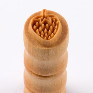 Könnte beinhalten: Ein Holzstempel mit Erdbeermuster. Der Stempel hat einen runden Griff und eine detaillierte Erdbeerschnitzerei auf der Oberseite. Das Holz ist hellbraun und der Stempel ist auf weißem Hintergrund gestapelt.