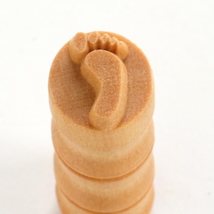 May include: A wooden stamp with a footprint design. The stamp is made of light brown wood and has a rounded top.