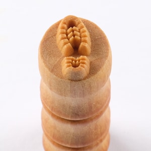 May include: A wooden stamp with a stacked handle. The top of the stamp features a detailed imprint of a shoe tread. The stamp is made of light-colored wood and is designed for imprinting on paper or other surfaces. The stamp is a craft supply.