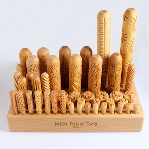 Könnte beinhalten: Ein Satz aus Holzwerkzeugen für die Töpferei in verschiedenen Designs und Größen. Die Werkzeuge sind in einem Holzgestell angeordnet, auf dem vorne der Text "MKM Pottery Tools TC-01" steht.