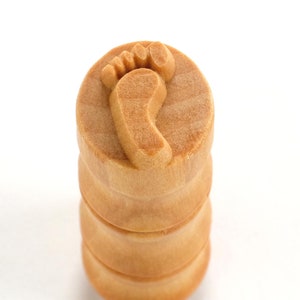 May include: A wooden stamp with a footprint design. The stamp is made of natural wood and has a light brown color.