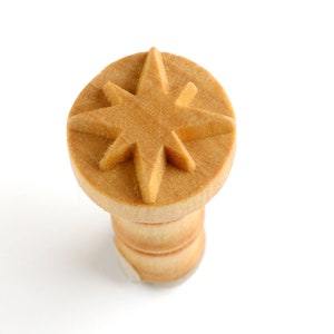 May include: A wooden stamp with a star-shaped design. The stamp is light brown and has a raised star design.