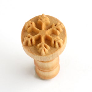 May include: A wooden snowflake cookie stamp with a brown handle.