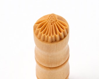 May include: A wooden stamp with a carved flower design. The stamp is cylindrical and has a light brown color.