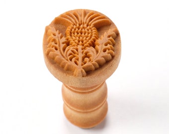 May include: A wooden stamp with a detailed carving of a thistle flower. The stamp is mounted on a wooden handle.