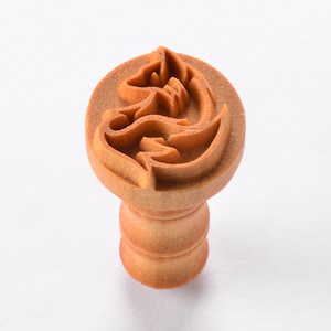 Peut inclure: Un emporte-pièce en bois avec un motif de deux poissons entrelacés. L'emporte-pièce est de couleur marron et a un dessus rond avec une base cylindrique.