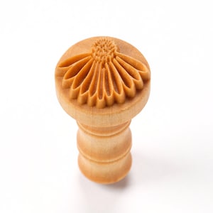 May include: A wooden stamp with a detailed floral design. The stamp is light brown and has a cylindrical handle.
