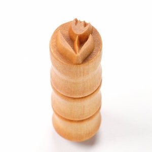 Könnte beinhalten: Ein Nudelholz aus Holz mit einem Tulpenmuster auf der Oberseite. Das Nudelholz ist aus hellbraunem Holz gefertigt und hat eine glatte Oberfläche.