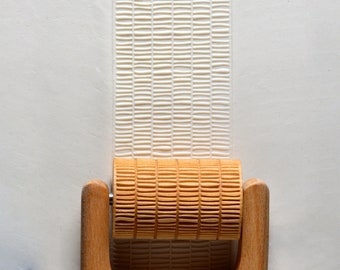 May include: A wooden rolling pin with a textured surface. The rolling pin is used to create a patterned design on clay or dough.