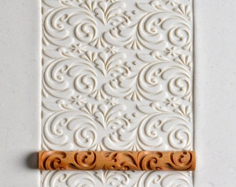 May include: A close-up of a white rolling pin with a decorative pattern. The rolling pin is made of silicone and has a wooden handle. The rolling pin is used to create decorative patterns in fondant or dough.