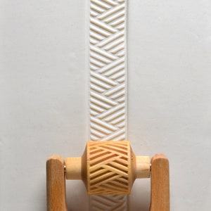 May include: A wooden rolling pin with a carved chevron pattern on the roller. The rolling pin has wooden handles and is used for creating decorative patterns in dough.