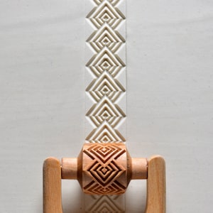 May include: A wooden rolling pin with a geometric pattern carved into the surface. The rolling pin is used to create decorative patterns in dough.