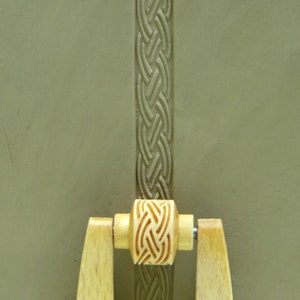 May include: A wooden rolling pin with a carved Celtic knot design. The rolling pin is used for creating decorative patterns in clay or dough.