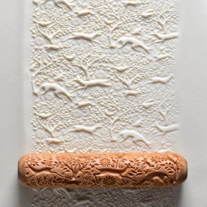May include: A wooden rolling pin with a detailed design of trees and animals. The rolling pin is used to create decorative patterns in dough.