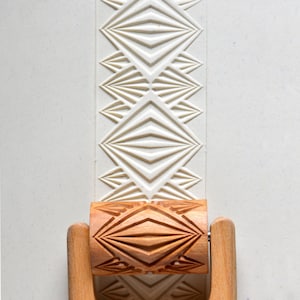 May include: A wooden rolling pin with a carved diamond pattern. The rolling pin is used to create decorative patterns in clay or dough.