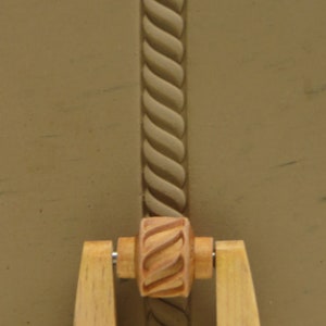 May include: A wooden rolling pin with a rope design. The rolling pin has two wooden handles and a central roller with a rope design.