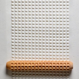 May include: A brown wooden rolling pin with a square pattern on the surface. The rolling pin is on a white background with a square pattern.