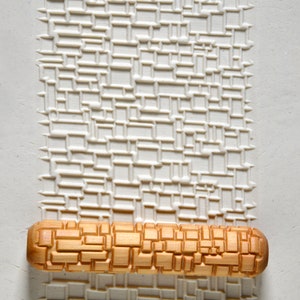 Peut inclure: Un rouleau à pâtisserie en bois avec un motif géométrique gravé à la surface. Le rouleau à pâtisserie est sur un fond blanc avec un motif géométrique similaire.