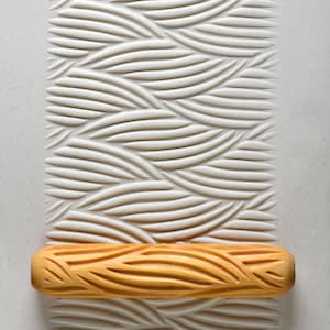 May include: A wooden rolling pin with a carved pattern of wavy lines. The rolling pin is lying on a white surface with a similar pattern embossed into it.