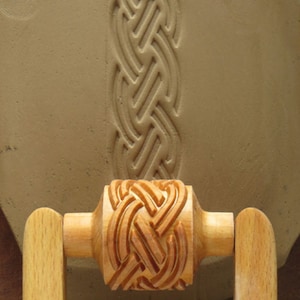 May include: A wooden rolling pin with a carved Celtic knot design. The rolling pin is used to create decorative patterns in clay.