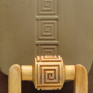 May include: A wooden rolling pin with a decorative design of repeating squares. The rolling pin has wooden handles on either side.