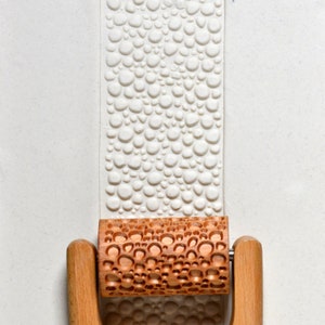 May include: A wooden rolling pin with a pattern of small circles, used for creating textured designs in clay or dough.
