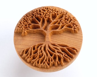 May include: A wooden round stamp with a detailed carving of a tree of life design. The tree has a thick trunk and branches with intricate details, and the roots are spread out in a circular pattern.
