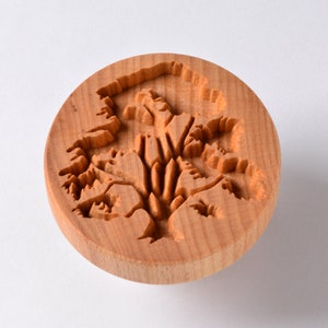 May include: A round wooden stamp with a carved design of a tree with branches and leaves.