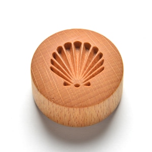 May include: A round wooden cookie cutter with a seashell design. The cutter is made of light brown wood and has a smooth, polished finish.