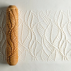 May include: A wooden rolling pin with a detailed fern pattern carved into the surface. The rolling pin is used to create an embossed design on fondant or dough.