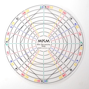 May include: A clear, circular 10-inch decorating disk with a grid pattern. The disk features concentric circles and intersecting lines in black, with colored markings in red, blue, yellow, and green. Text includes "MKM 10IN DECORATING Disk".