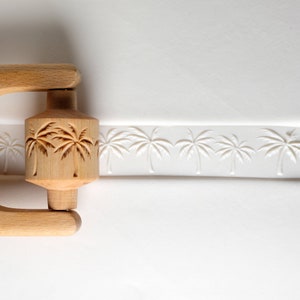 May include: A wooden rolling pin with a palm tree design. The rolling pin is used to create an embossed pattern on fondant or dough.
